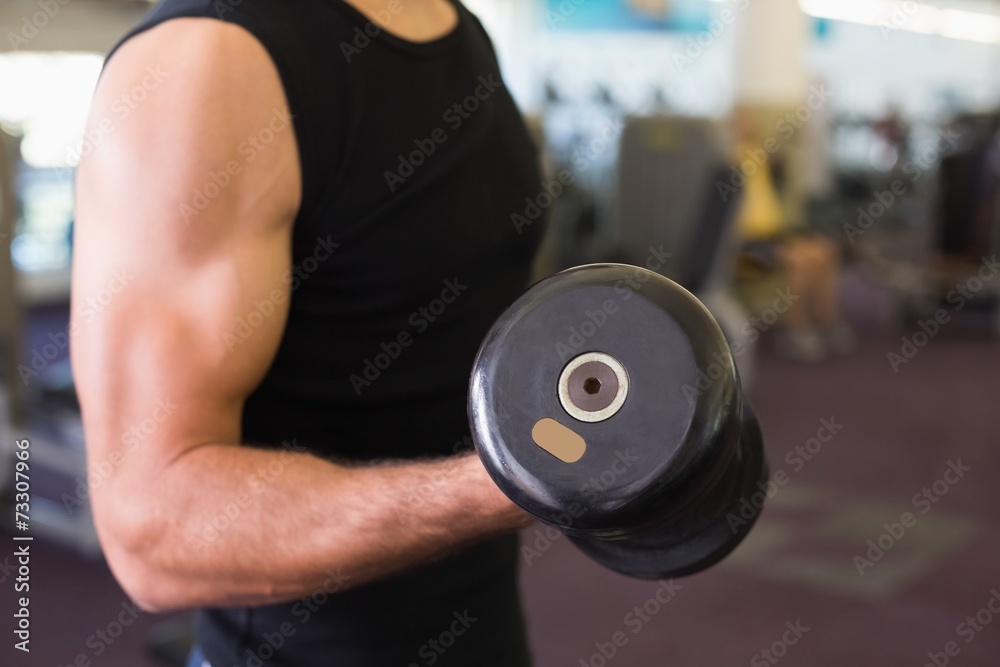 Mid section of man exercising with dumbbell in gym Mid section of man exercising with dumbbell in gym