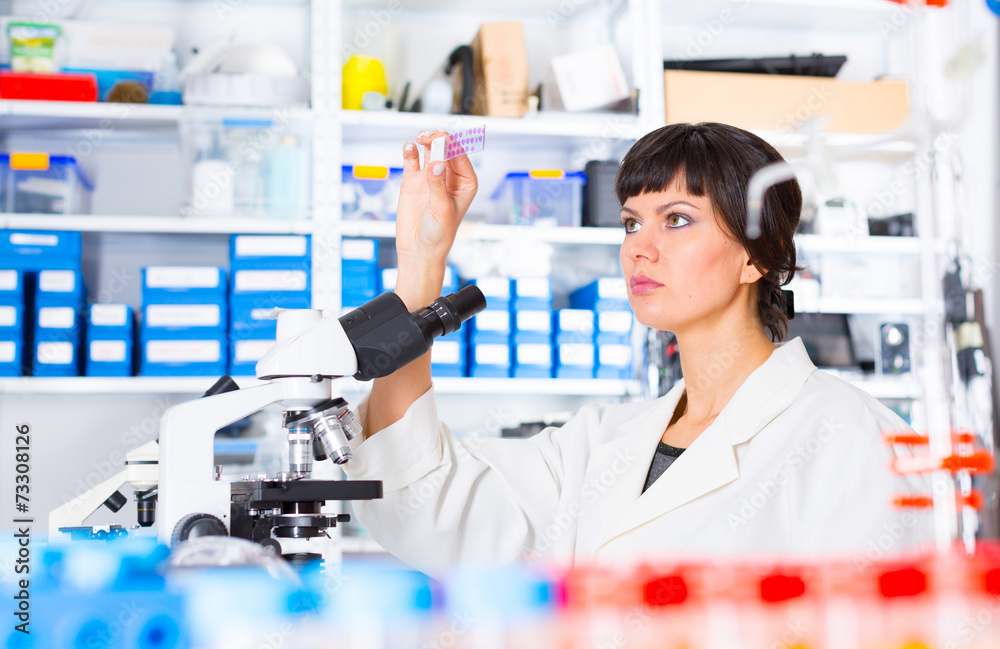 woman in a laboratory microscope with microscope slide in hand woman in a laboratory microscope with microscope slide in hand