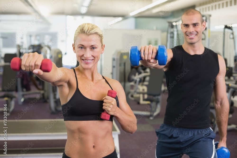 Couple exercising with dumbbells in gym Couple exercising with dumbbells in gym