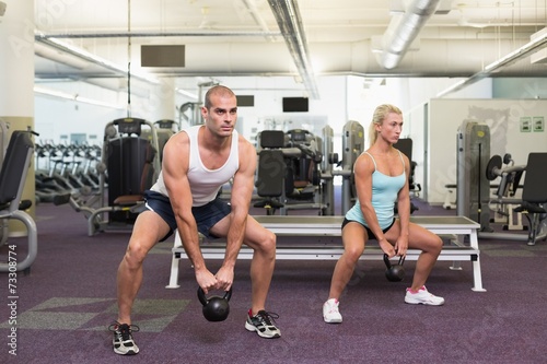 Fit couple lifting kettle bells in gym