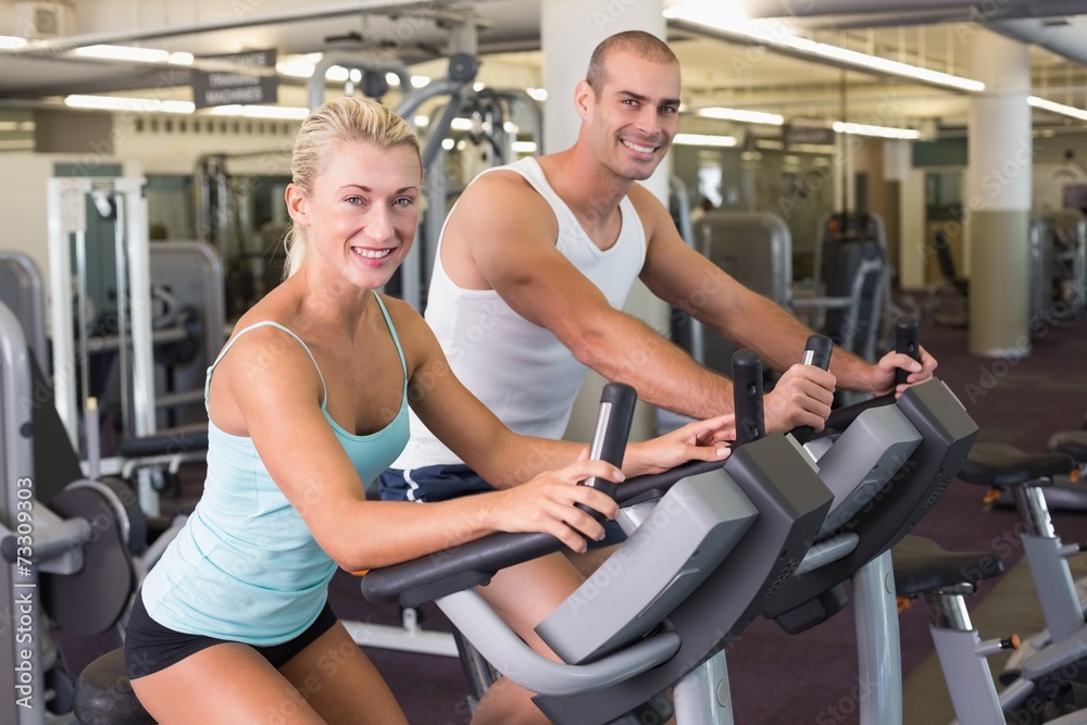 Fit young couple working on exercise bikes at gym Fit young couple working on exercise bikes at gym