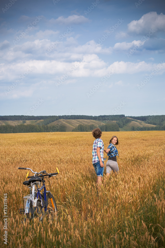Teenage girl and boy on a bicycle in a summer field of rye