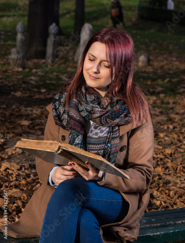 Redhead girl sitting on bench in park and reading book