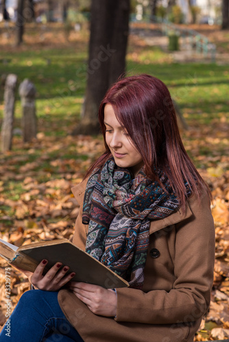 redhead girl sitting on bench in park and reading book