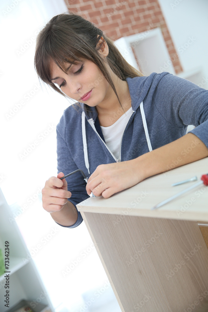 Single young woman assembling pieces of new furniture Single young woman assembling pieces of new furniture