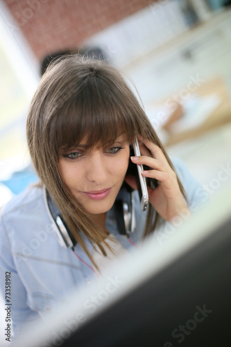 Young woman talking on smartphone in front of desktop