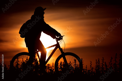 Велосипедист на берегу реки на закате Солнца
