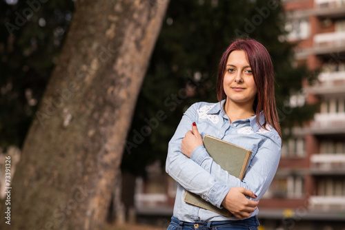Redhead girl standing and holding a book in park