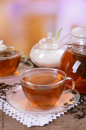 Teapot and cups of tea on table on light background