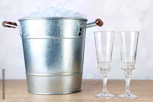 Ice bucket and two glasses on wooden table on light background