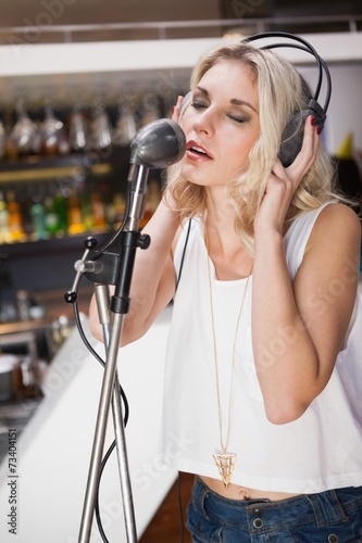 Pretty blonde with headphone singing into microphone