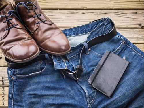 detail of blue jeans with black leather belt shoes and notebook