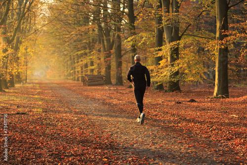 Man trail running in a autumn colored lane in the forest. photo