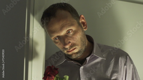 Sad man smelling rose and standing next to the window
