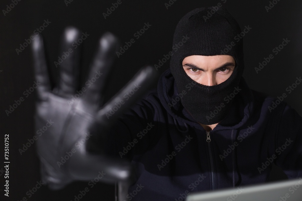 Hacker in balaclava gesturing and looking at camera Hacker in balaclava gesturing and looking at camera