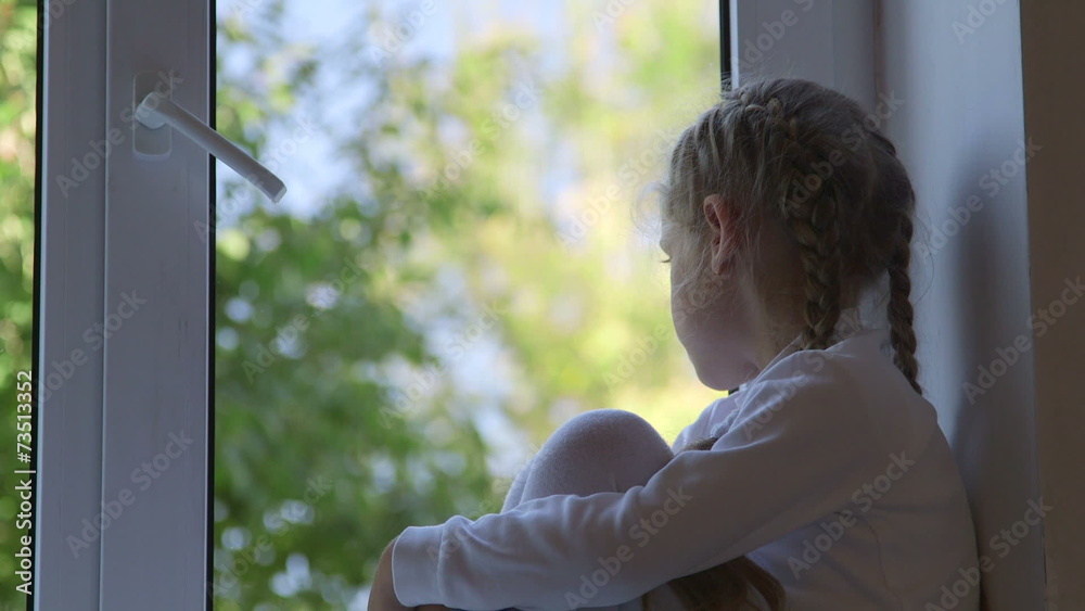 Little girl sitting on windowsill and looking out the window