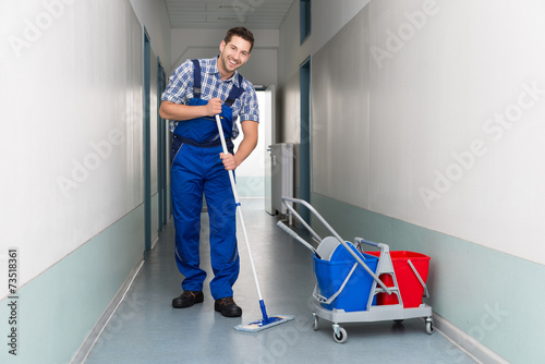 Happy Male Worker With Broom Cleaning Office Corridor