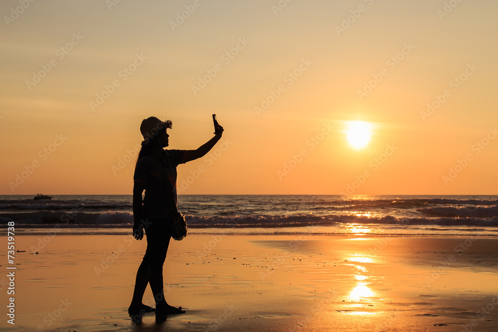 Silhouette of Thai Woman using smartphone at the beach in sunset