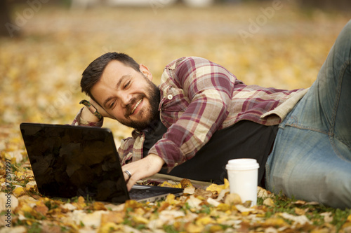 Man Laying Down In Autumn Leaves Using Laptop Computer