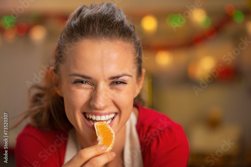 Portrait of young housewife eating orange in kitchen