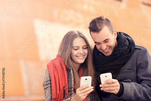 Young couple sitting on a bench and using smartphones