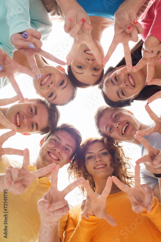 group of smiling teenagers showing victory sign
