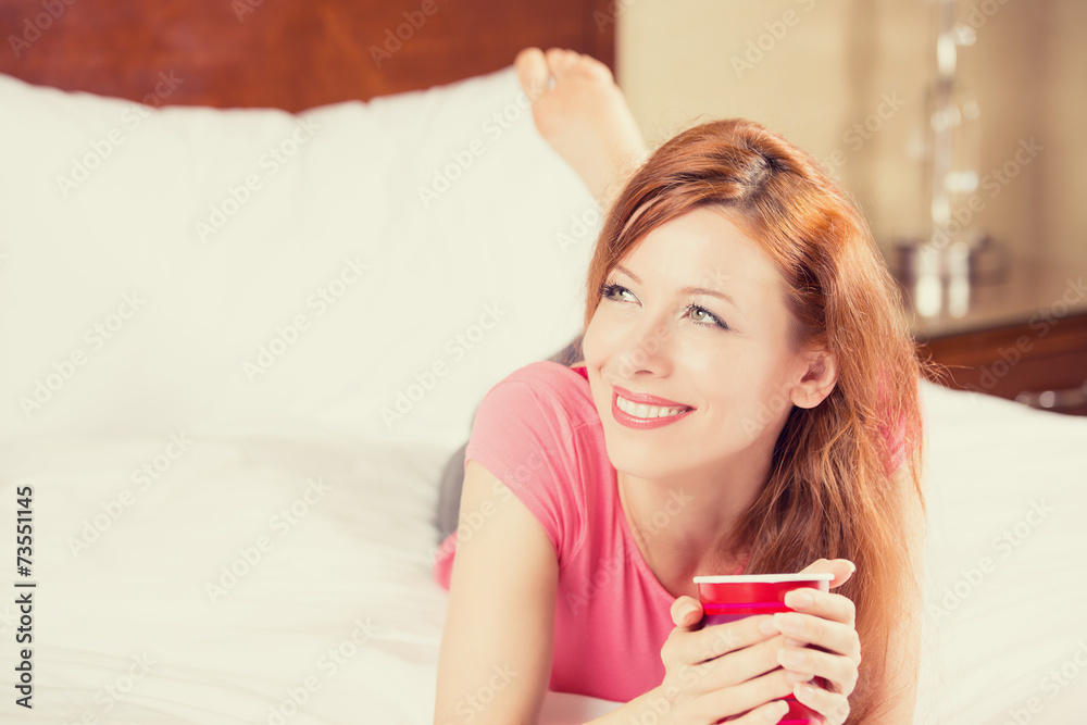 smiling woman lying in bed drinking her morning coffee smiling woman lying in bed drinking her morning coffee