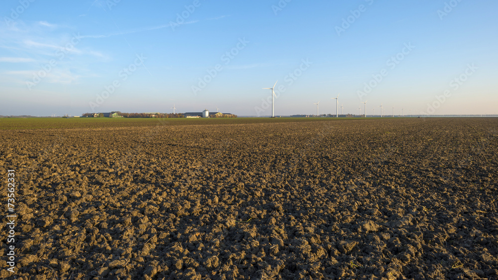 Wind farm along a plowed field at sunset in autumn Wind farm along a plowed field at sunset in autumn