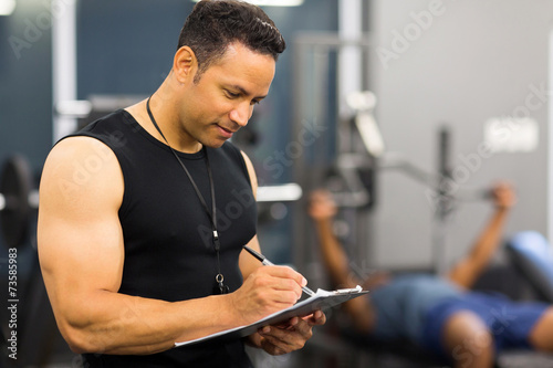 mid age male gym trainer writing on clipboard