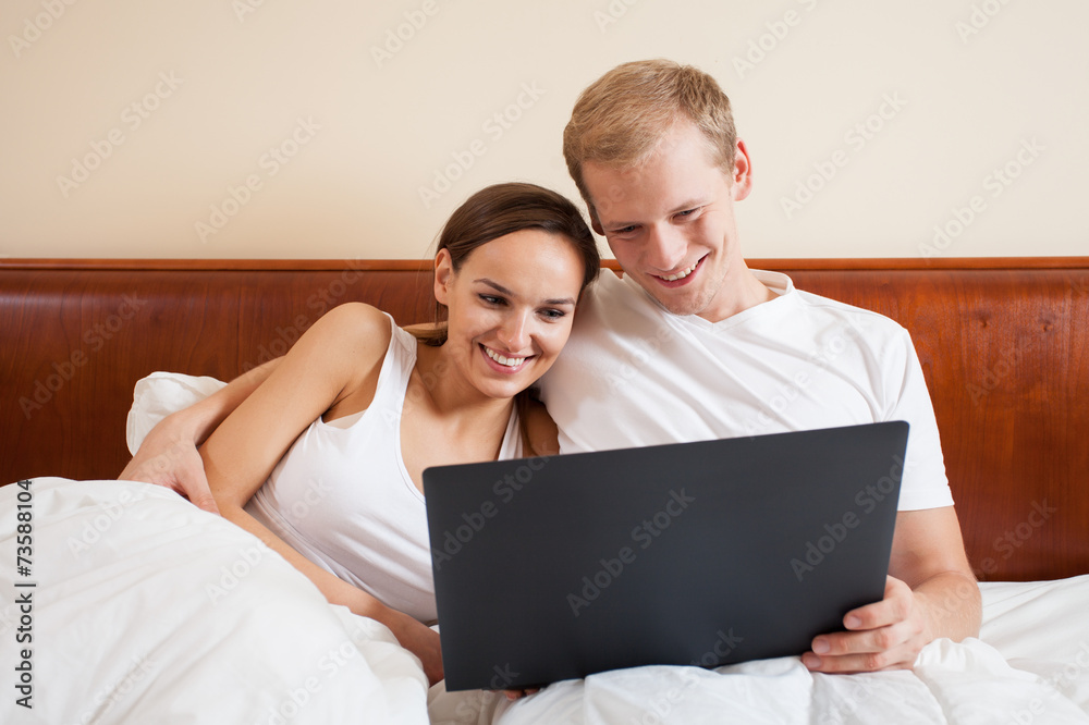 Happy couple in bed with laptop