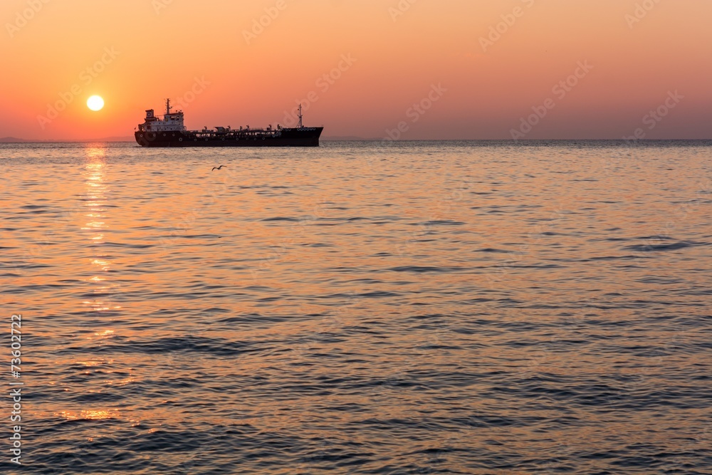 Fototapeta premium Sunset at the sea with cargo ship