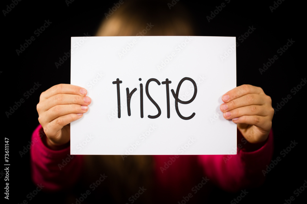 Child holding sign with Spanish word Triste - Sorry Child holding sign with Spanish word Triste - Sorry