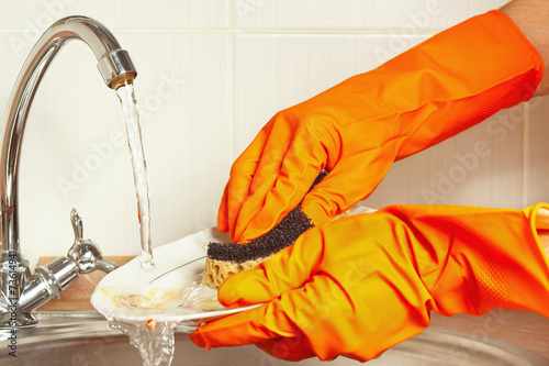 Hands in gloves wash dishes under running water in kitchen photo