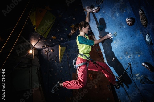 Young woman practicing rock-climbing on a rock wall indoors