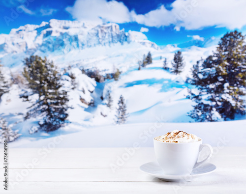 cup of cappuccino with whipped cream over winter landscape
