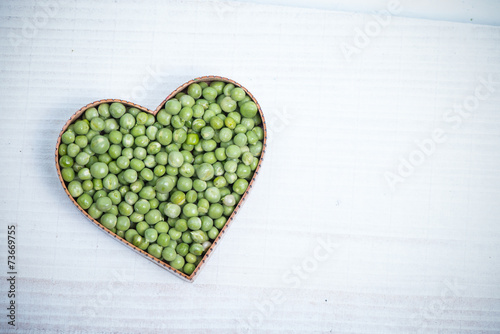 heart shape with fresh green peas on white table