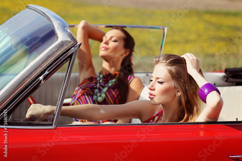 Beautiful ladies with sun glasses posing in a vintage car