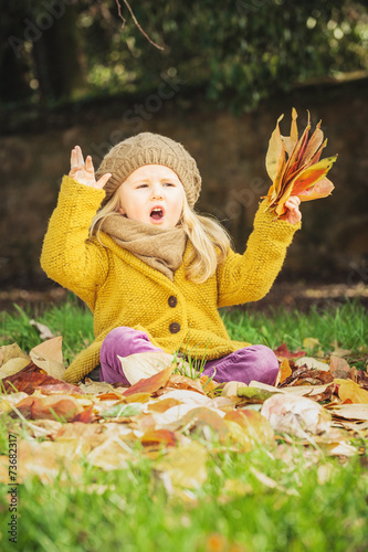 Beautiful girl  smiling blonde plays with the autumn leaves