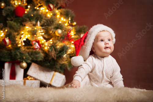 Happy baby wearing Santa hat over christmas tree © julenochek
