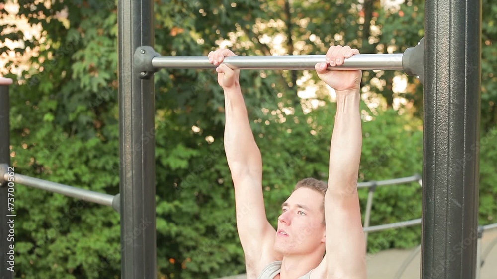 Young muscular man in tank top doing knee to bar at park during Young muscular man in tank top doing knee to bar at park during