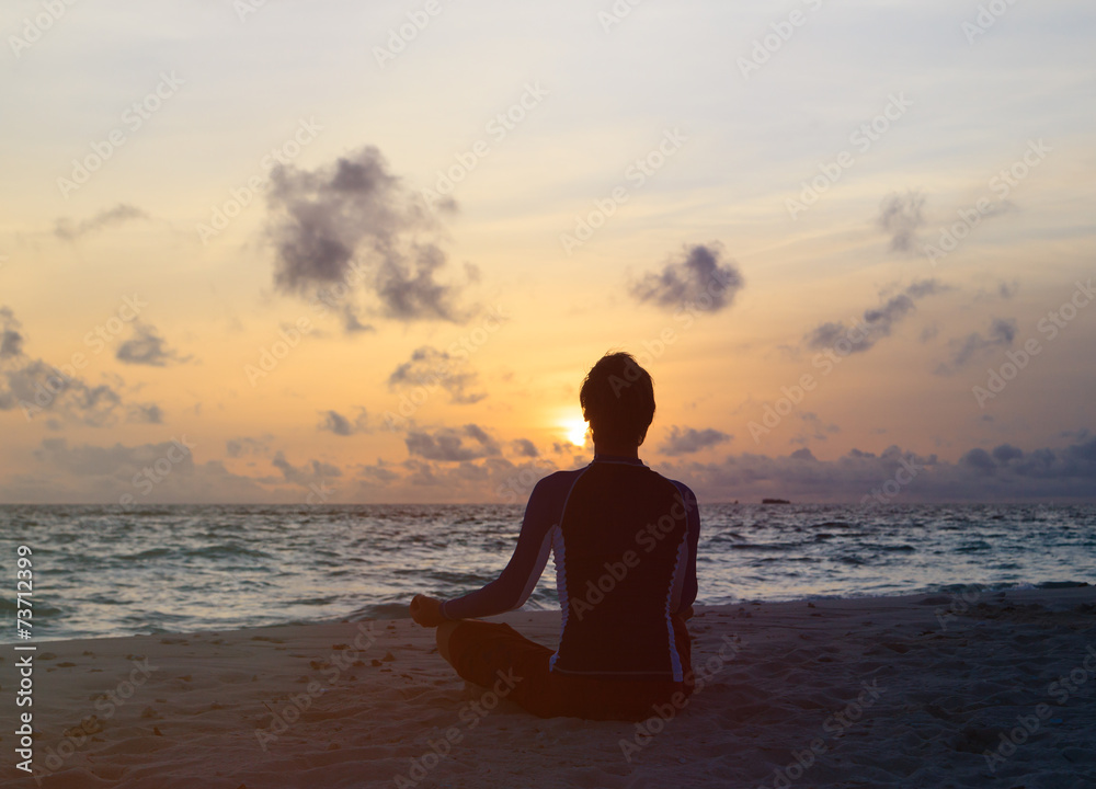 Silhouette of man meditating at sunset beach