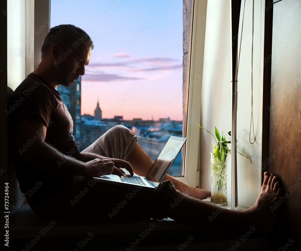 Silhouette of man on window sill with laptop