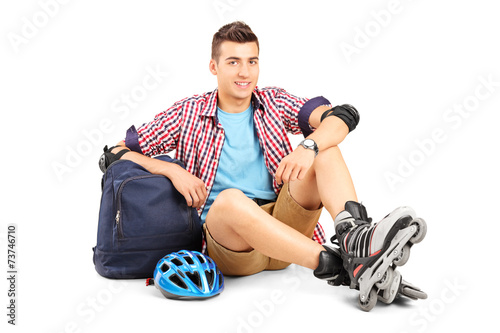 Young man with rollerblades sitting on the floor