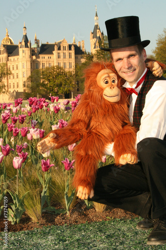 Zauberer und Bauchredner mit Zylinderhut sitzt mit einem Affe als Puppe vor einem Tulpenbeet des Schweriner Schloss photo