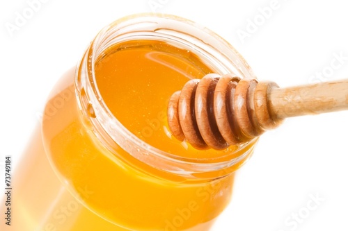 honey jar on white background with wooden honey dipper on top