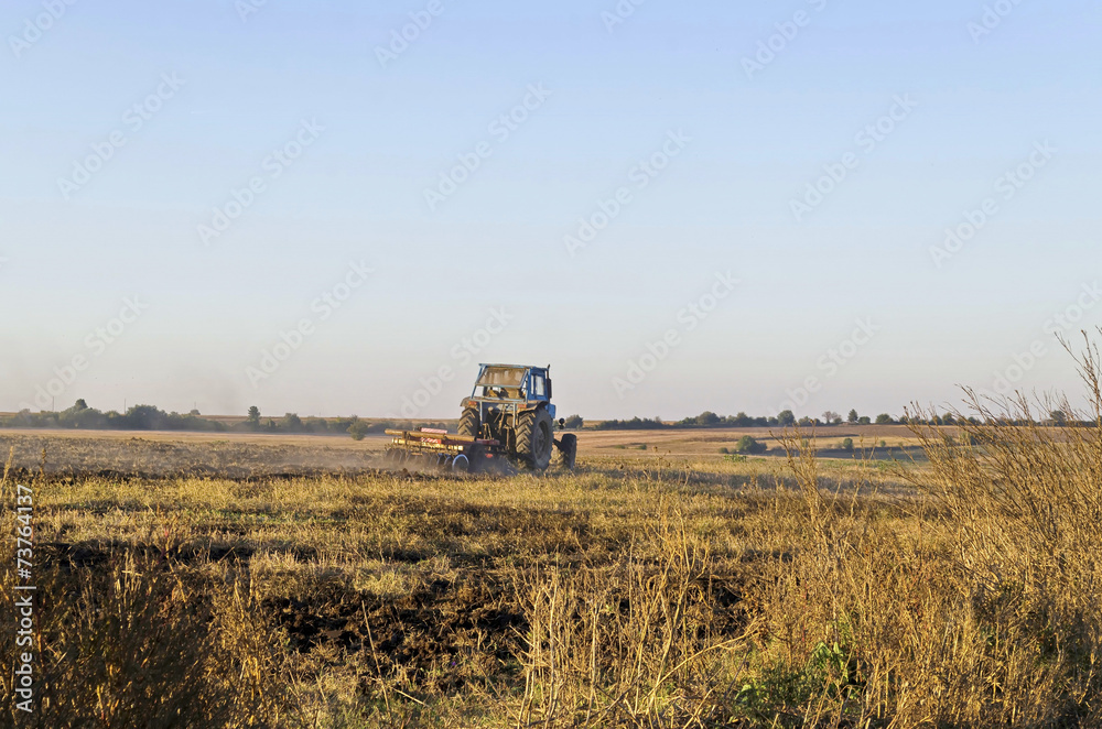 Fototapeta premium Tractor cultivating wheat stubble field with crop residue