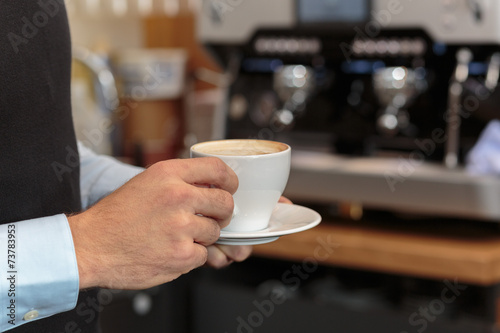 Männerhand hält Kaffee in Tasse vor Kaffee Maschine als Kulisse