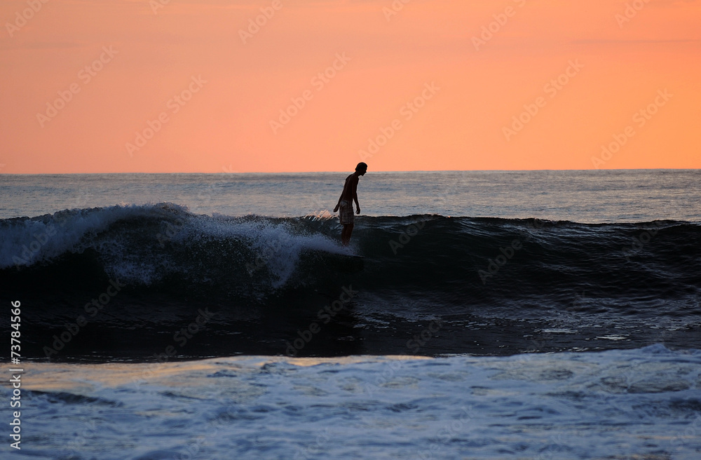 ein Surfer surft die letzte welle vor roter Abendsonne