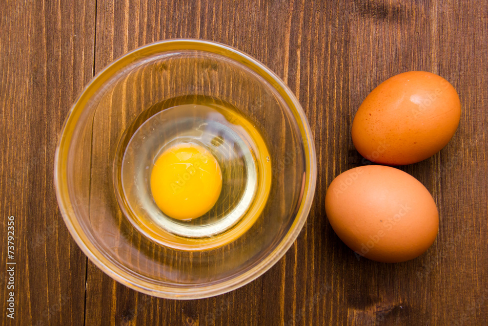 Open egg on bowl on wooden table seen from above Open egg on bowl on wooden table seen from above