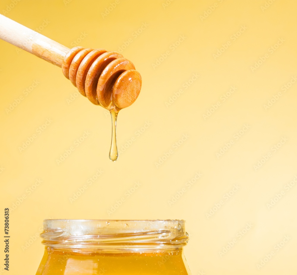 honey jar on golden background with wooden dipper on top honey jar on golden background with wooden dipper on top